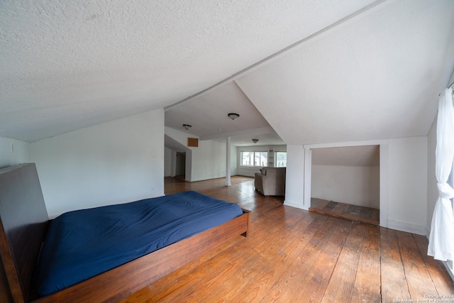 unfurnished bedroom featuring vaulted ceiling, a textured ceiling, and hardwood / wood-style flooring