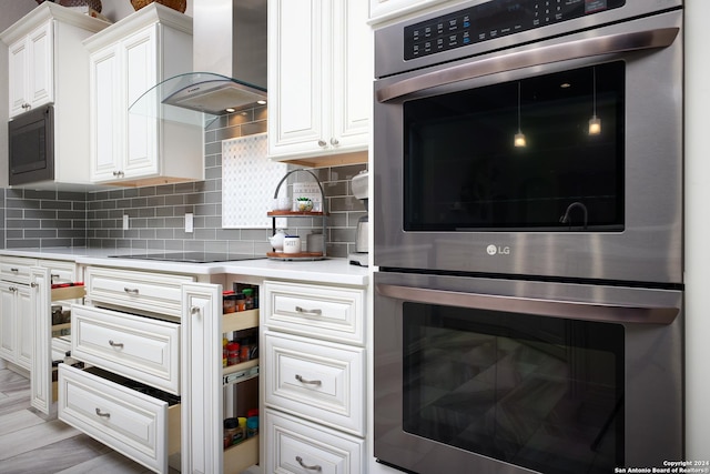 kitchen with white cabinetry, stainless steel double oven, tasteful backsplash, built in microwave, and wall chimney exhaust hood