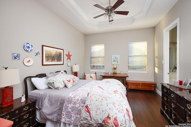 bedroom featuring ceiling fan, connected bathroom, a tray ceiling, dark wood-type flooring, and ornamental molding