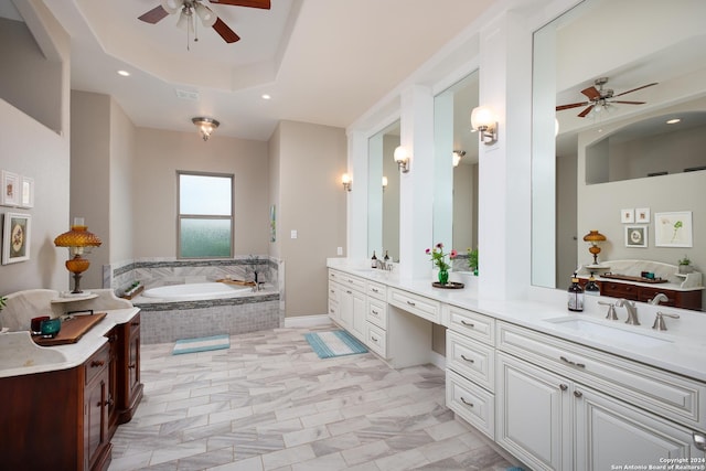 bathroom featuring ceiling fan, a relaxing tiled tub, a raised ceiling, and vanity