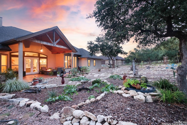 yard at dusk featuring ceiling fan, french doors, and a patio