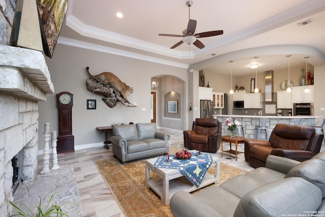 living room featuring ceiling fan, a fireplace, crown molding, and a tray ceiling