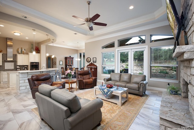 living room featuring ceiling fan, ornamental molding, a fireplace, and a raised ceiling