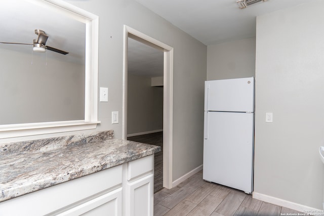 kitchen featuring ceiling fan, light stone countertops, white cabinets, and white fridge