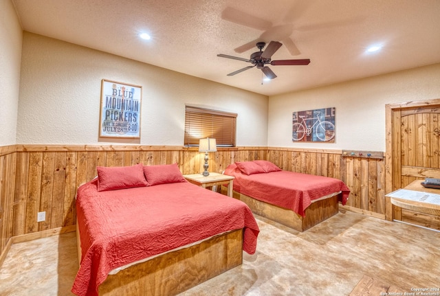 bedroom with ceiling fan, a textured ceiling, light carpet, and wooden walls