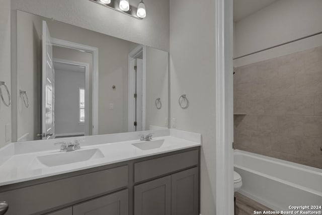 full bathroom with wood-type flooring, tiled shower / bath combo, vanity, and toilet