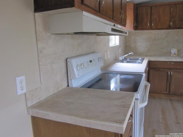 kitchen with a sink, light wood-style floors, light countertops, white range with electric stovetop, and decorative backsplash