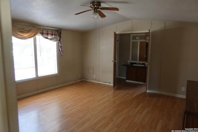 empty room featuring ceiling fan, a textured ceiling, lofted ceiling, a sink, and light wood-type flooring