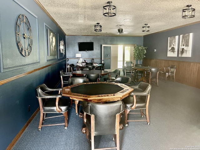 carpeted dining room with a textured ceiling, wooden walls, a ceiling fan, wainscoting, and crown molding