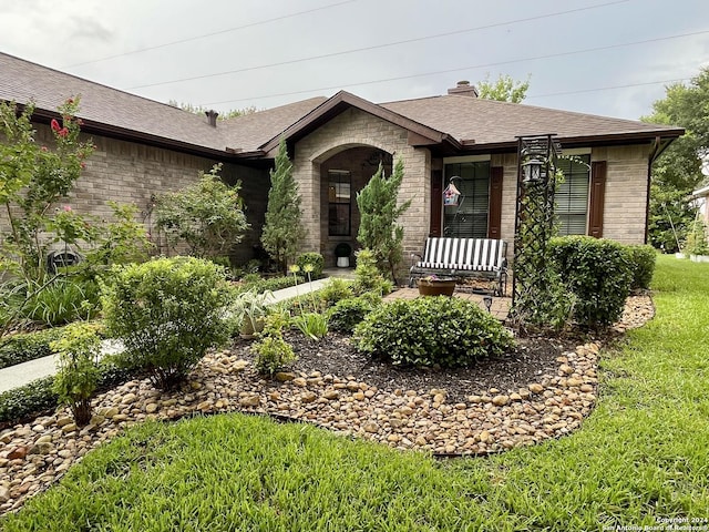 view of front facade featuring a front yard, brick siding, a chimney, and roof with shingles