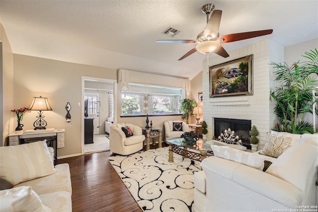 living area featuring visible vents, dark wood finished floors, vaulted ceiling, a textured ceiling, and a fireplace