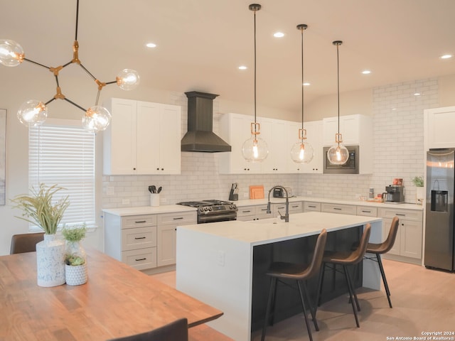 kitchen featuring gas range oven, stainless steel fridge, wall chimney range hood, sink, and backsplash