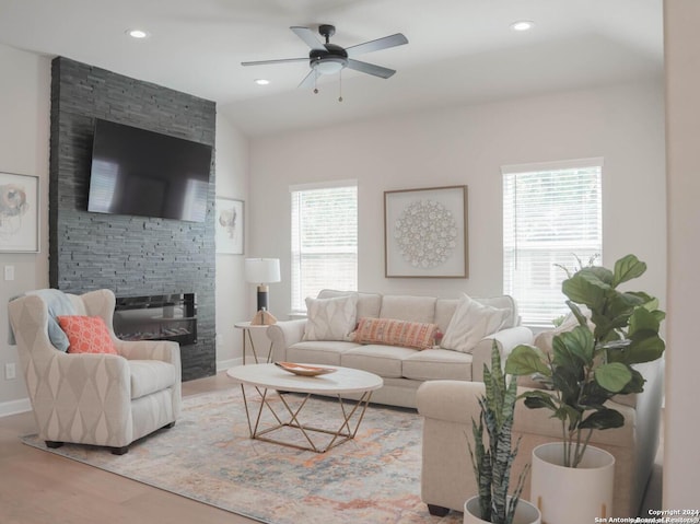 living room with ceiling fan, a stone fireplace, and hardwood / wood-style floors