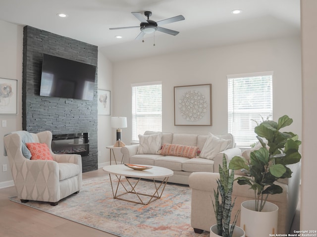 living room with a stone fireplace, wood-type flooring, and ceiling fan