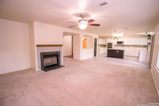 unfurnished living room featuring ceiling fan, a fireplace, light colored carpet, and sink