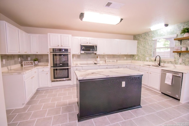 kitchen featuring light stone countertops, white cabinetry, sink, stainless steel appliances, and a kitchen island