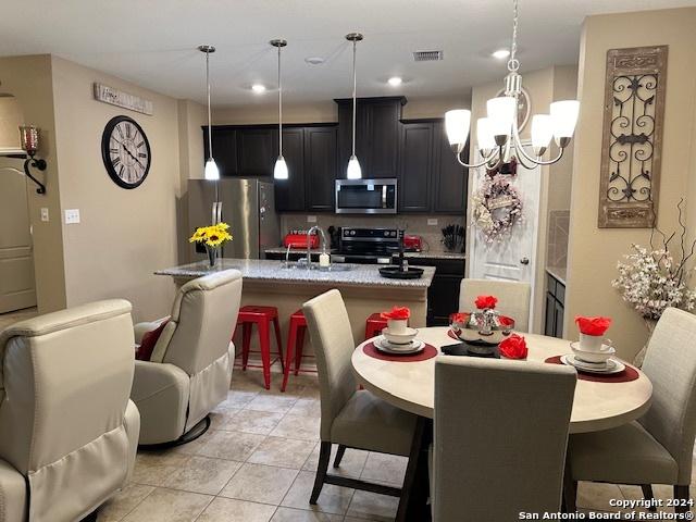 kitchen featuring a kitchen island with sink, hanging light fixtures, stainless steel appliances, a kitchen breakfast bar, and light stone countertops