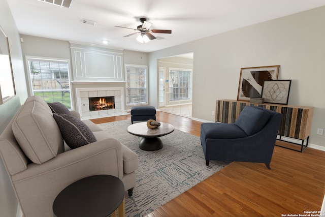 living room with light hardwood / wood-style floors, a tile fireplace, and ceiling fan