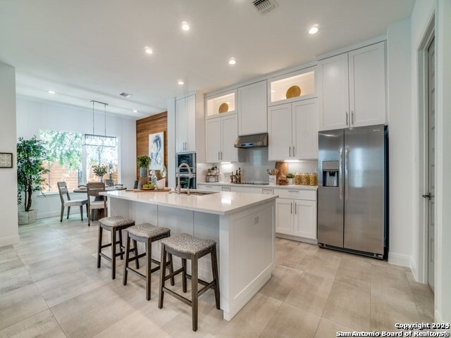 kitchen featuring stainless steel fridge, sink, hanging light fixtures, a kitchen island with sink, and white cabinetry