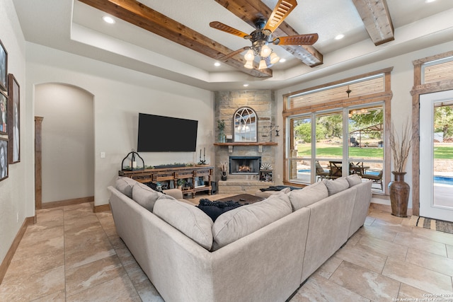 living room with a stone fireplace, ceiling fan, a raised ceiling, and light tile patterned floors