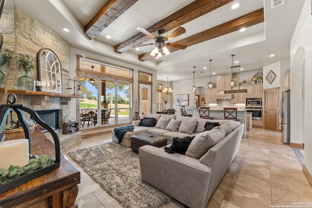 tiled living room featuring a stone fireplace, beamed ceiling, ceiling fan with notable chandelier, and a raised ceiling