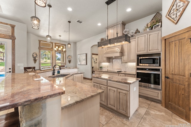 kitchen featuring light stone counters, a large island, appliances with stainless steel finishes, decorative light fixtures, and sink