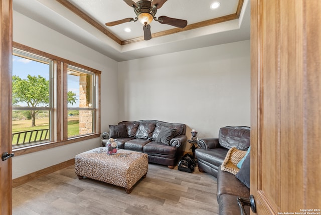 living room with light hardwood / wood-style floors, ceiling fan, plenty of natural light, and a tray ceiling