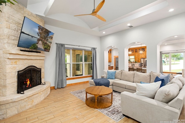 living room with ceiling fan, a fireplace, light hardwood / wood-style flooring, and a raised ceiling