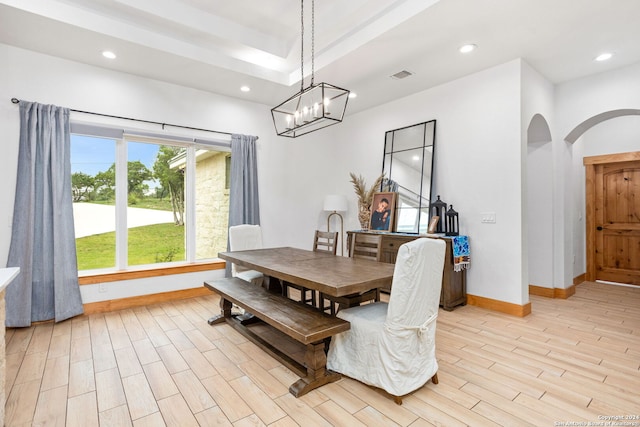 dining room with a tray ceiling, light hardwood / wood-style flooring, and an inviting chandelier