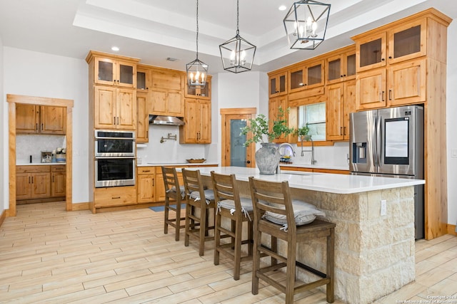 kitchen featuring a tray ceiling, a center island, a kitchen bar, appliances with stainless steel finishes, and backsplash