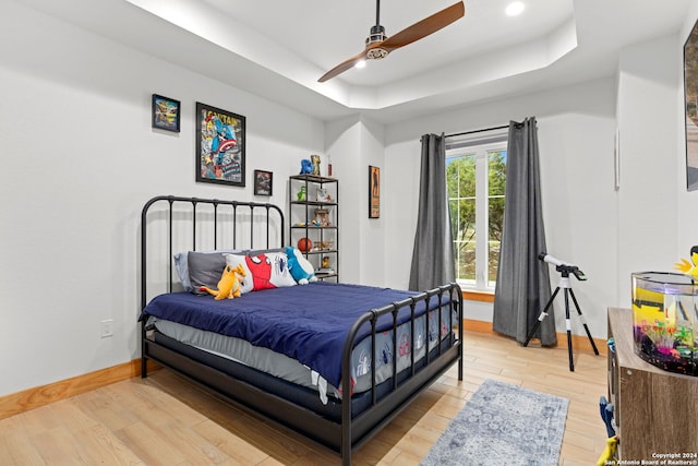 bedroom with ceiling fan, light wood-type flooring, and a tray ceiling