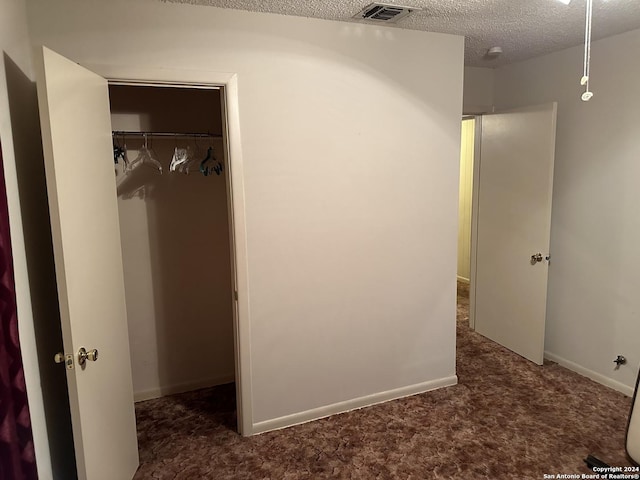 unfurnished bedroom featuring a closet, a textured ceiling, and dark colored carpet