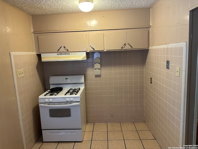 kitchen with white cabinetry, light tile patterned floors, a textured ceiling, gas range gas stove, and tile walls