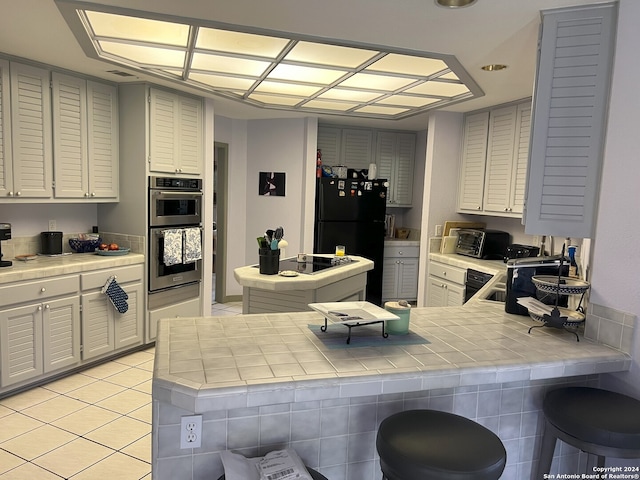 kitchen featuring double oven, freestanding refrigerator, light tile patterned flooring, and tile countertops