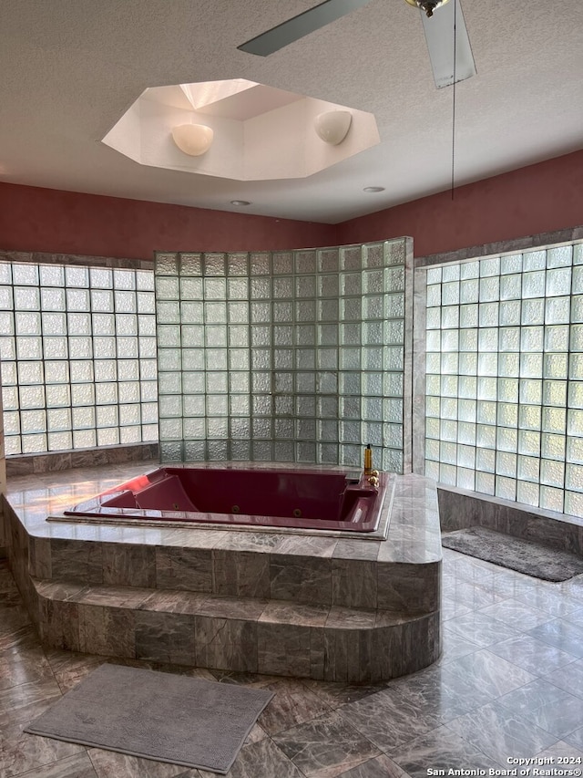 bathroom with a raised ceiling, tiled bath, a textured ceiling, and tile patterned floors