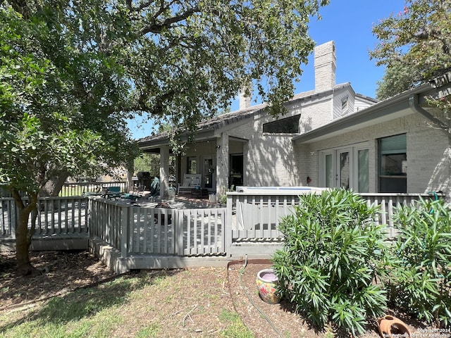 back of house with a deck, french doors, a chimney, and brick siding