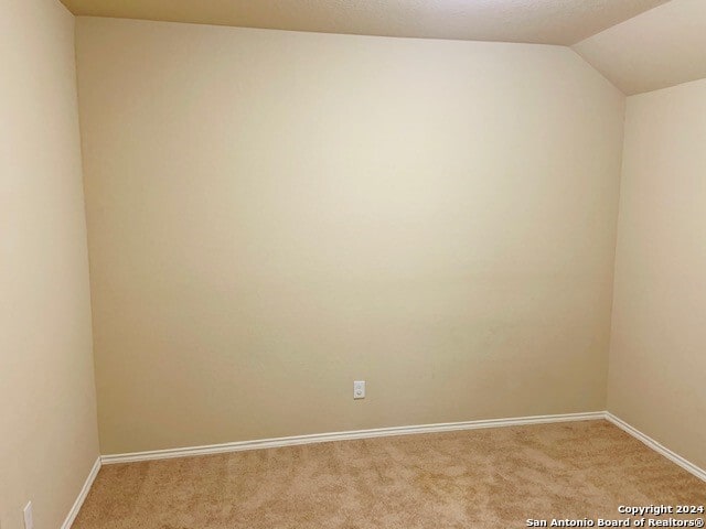 carpeted empty room with vaulted ceiling