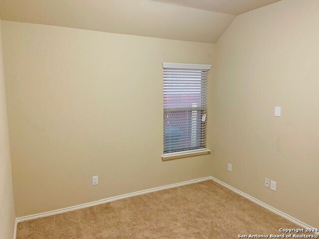 carpeted empty room with vaulted ceiling