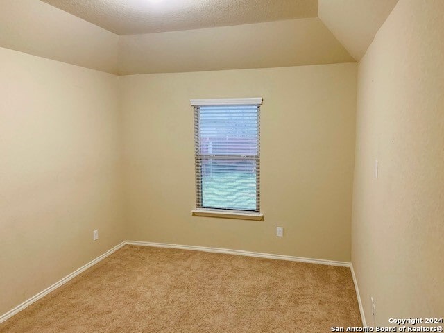 carpeted spare room featuring a textured ceiling and vaulted ceiling