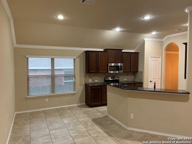 kitchen with light tile patterned flooring, tasteful backsplash, stainless steel appliances, crown molding, and kitchen peninsula