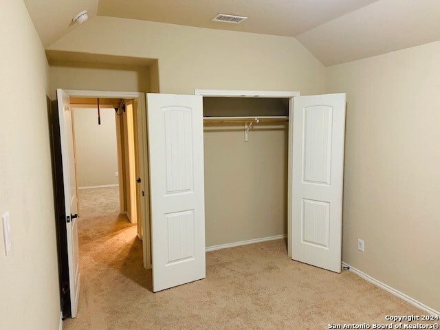 unfurnished bedroom featuring a closet, lofted ceiling, and light carpet