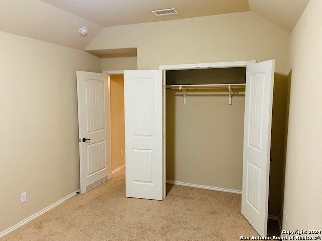 unfurnished bedroom with vaulted ceiling, light colored carpet, and a closet