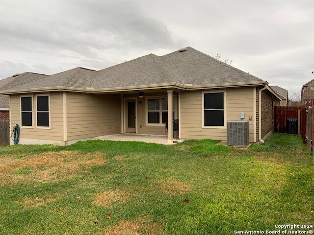 rear view of property with central AC, a patio area, and a lawn