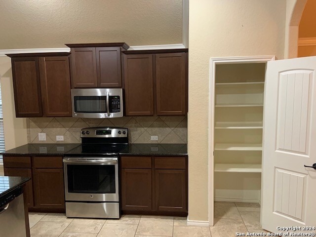 kitchen featuring dark stone counters, tasteful backsplash, stainless steel appliances, dark brown cabinets, and light tile patterned flooring