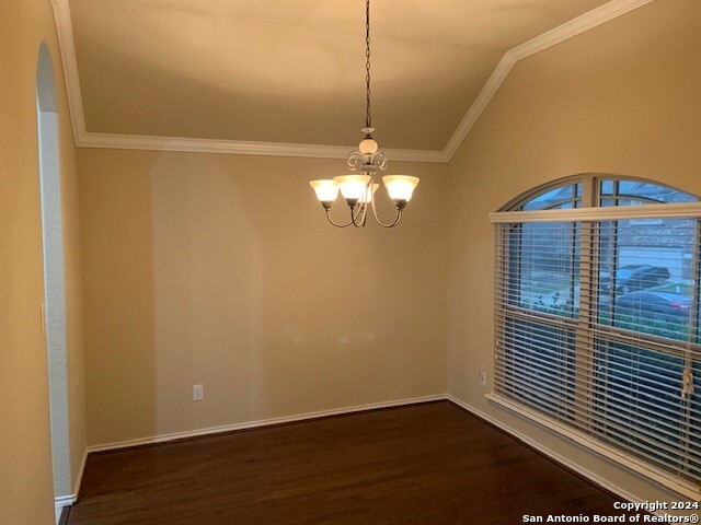 empty room featuring vaulted ceiling, a notable chandelier, hardwood / wood-style floors, and ornamental molding