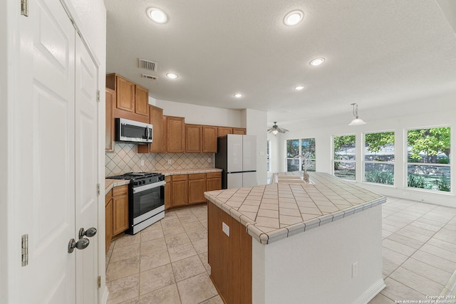 kitchen with a kitchen island with sink, stainless steel appliances, hanging light fixtures, sink, and decorative backsplash