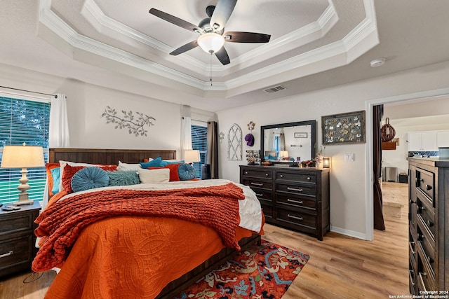 bedroom with ceiling fan, ornamental molding, light hardwood / wood-style floors, and a tray ceiling