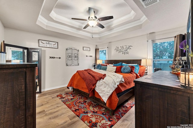 bedroom with light wood-type flooring, ceiling fan, crown molding, and a raised ceiling