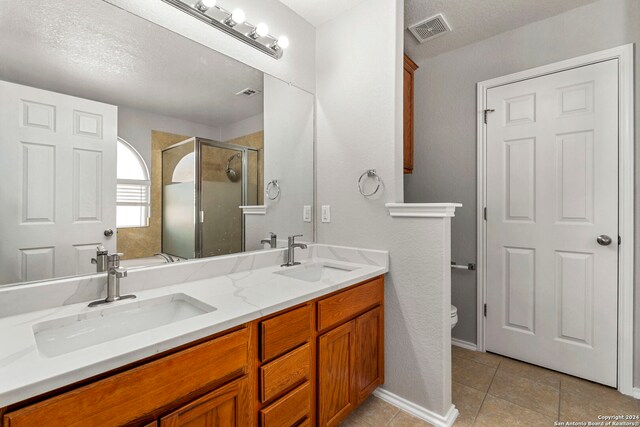 bathroom featuring toilet, tile patterned floors, a textured ceiling, and double vanity