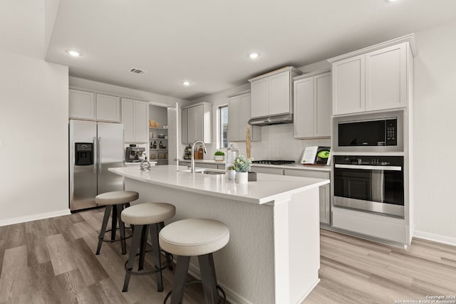 kitchen with sink, light hardwood / wood-style flooring, an island with sink, a kitchen bar, and appliances with stainless steel finishes